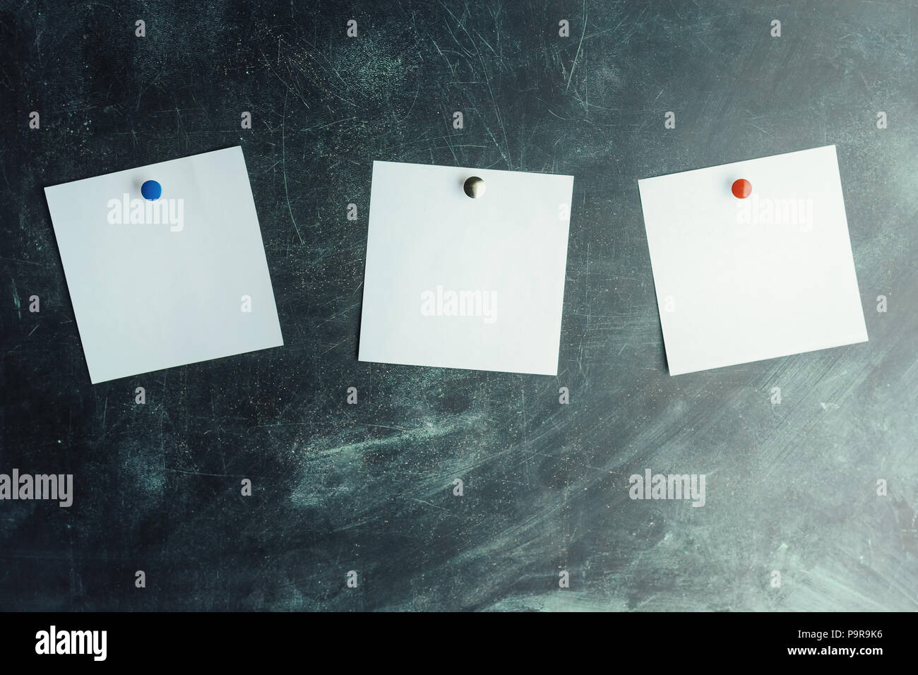 Three white stickers on dark board pinned with colored studs Stock Photo