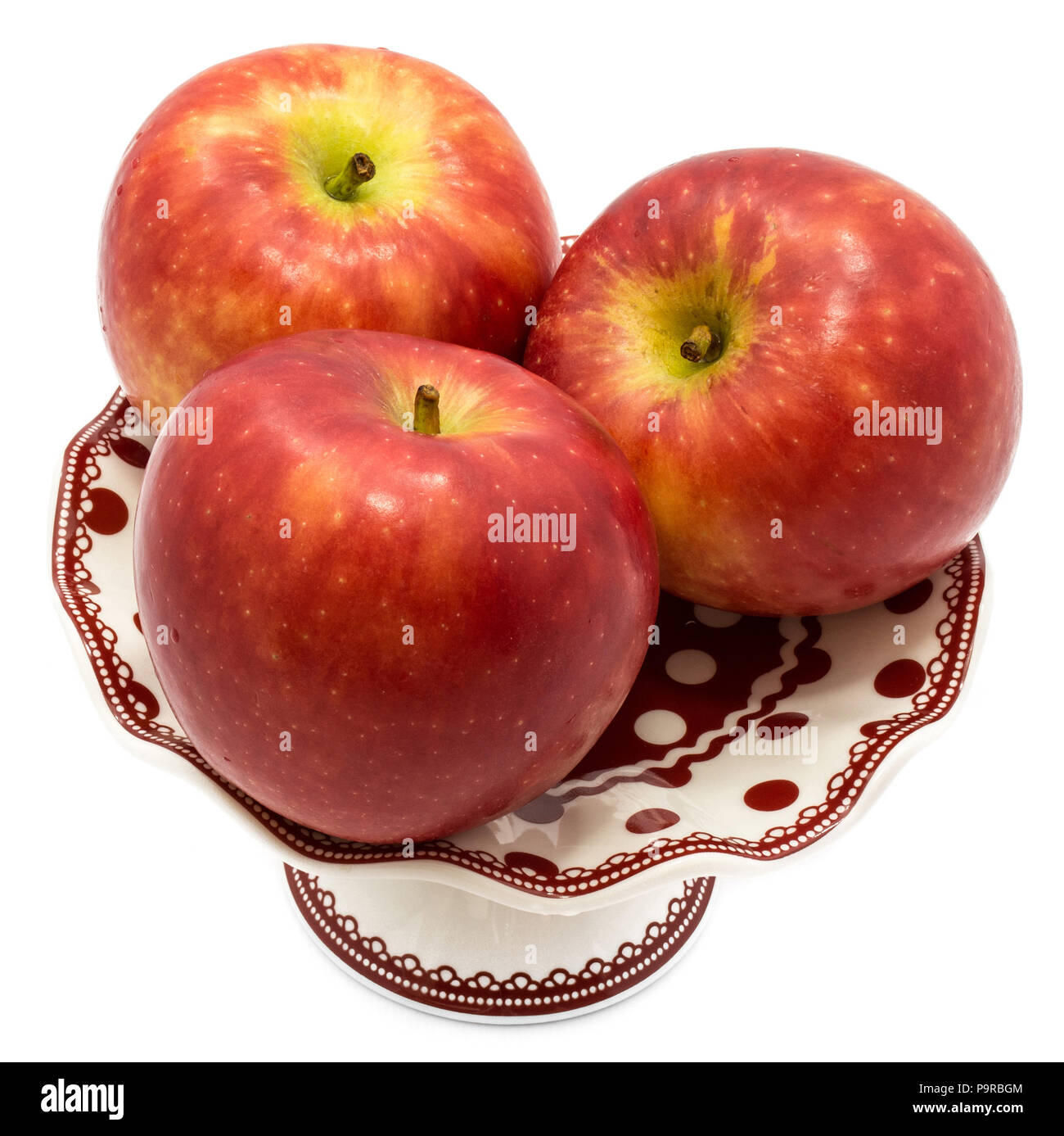 Three whole red Kanzi apples on plate isolated on white background
