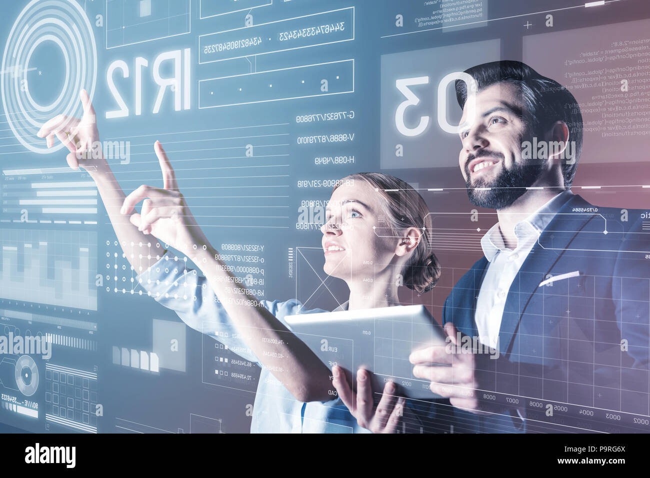 Smiling colleagues. Cheerful emotional skilled programmers smiling while standing in front of the screen and working at the new program Stock Photo