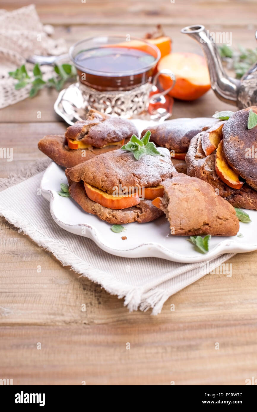 Homemade pastries with persimmons, for breakfast. Beautiful glass with tea. Kettle. A wooden table, a place for text or advertising Stock Photo