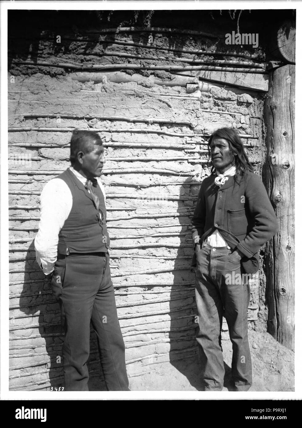 . English: Chief of the 'Friendly' Yuma Indians, John Townsend, and the interpreter, Poncho Lachero, ca.1900 Photograph of the Chief of the 'Friendly' Yuma Indians, John Townsend, and the interpreter, Poncho Lachero, ca.1900. They stand facing one another in front of the wall of a stick and mud dwelling with a thatched roof. The interpreter, with short hair, on the left, stands with his hands clasped behind his back. He is wearing a vest over a white shirt, with tie and trousers. The chief, with long hair, at right, stands with his hands thrust in the front pockets of his trousers. He also wea Stock Photo