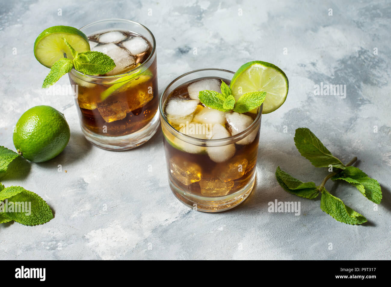 Rum and cola. Cuba Libre drink with lime and ice on rustic concrete table. Stock Photo