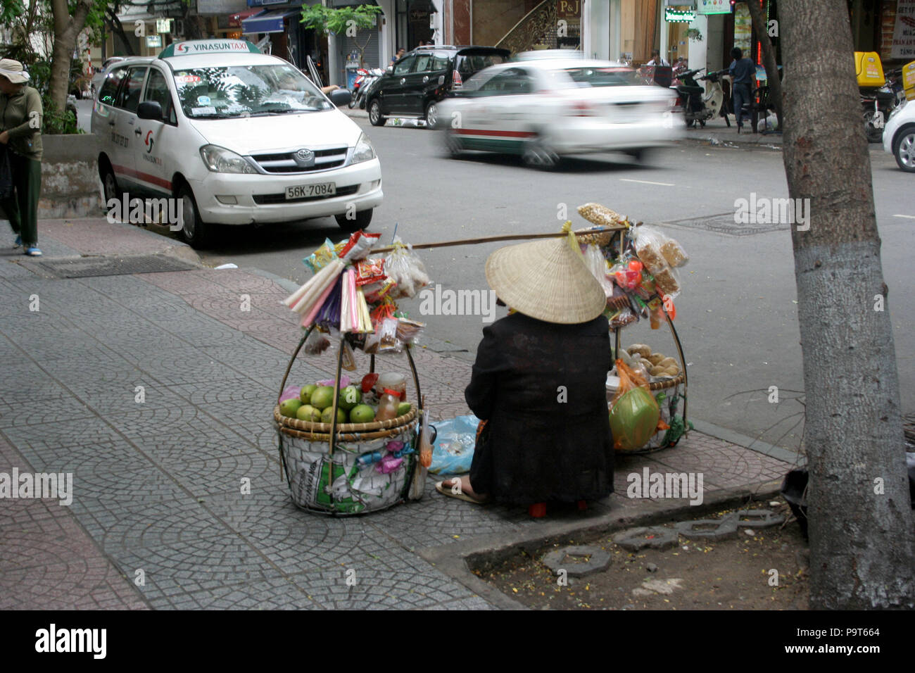 Vietnamese Lady in Conical Hat with Baskets of Fruit, Sitting on the Street, Ho Chi Minh City Stock Photo