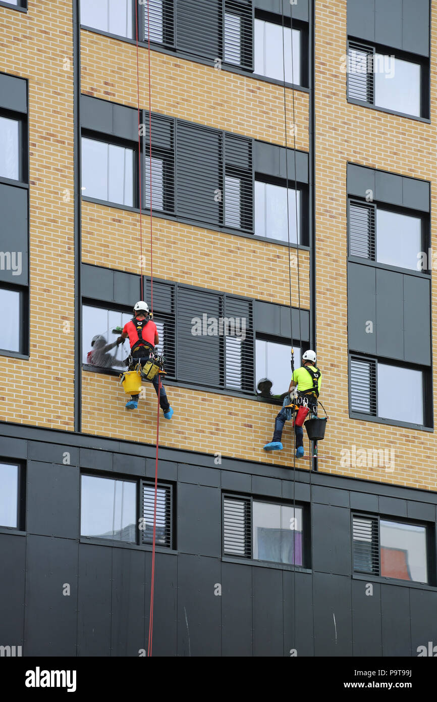 Two window cleaners use abseiling ropes to access windows on a new tower block in Portsmouth town centre, Hampshire, UK Stock Photo