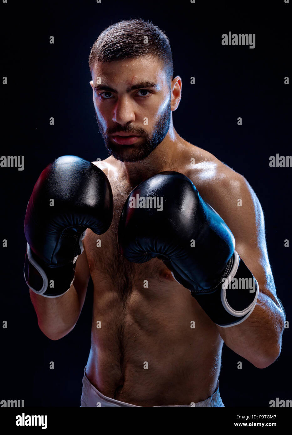 Strong muscular boxer in black boxing gloves. A man in a boxing stand