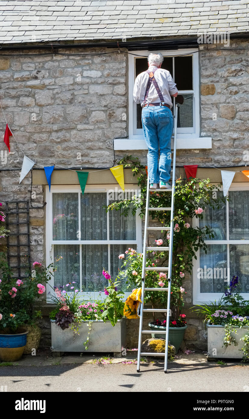 Man up a ladder working on the window of a cottage, Tideswell, Derbyshire Stock Photo