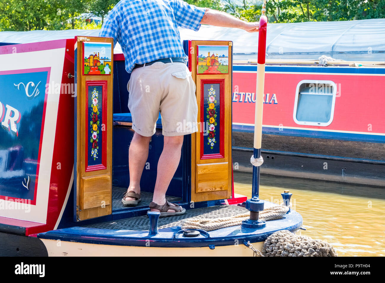 Man at the tiller of a narrowboat on the Macclesfield Canal. Cheshire Stock Photo