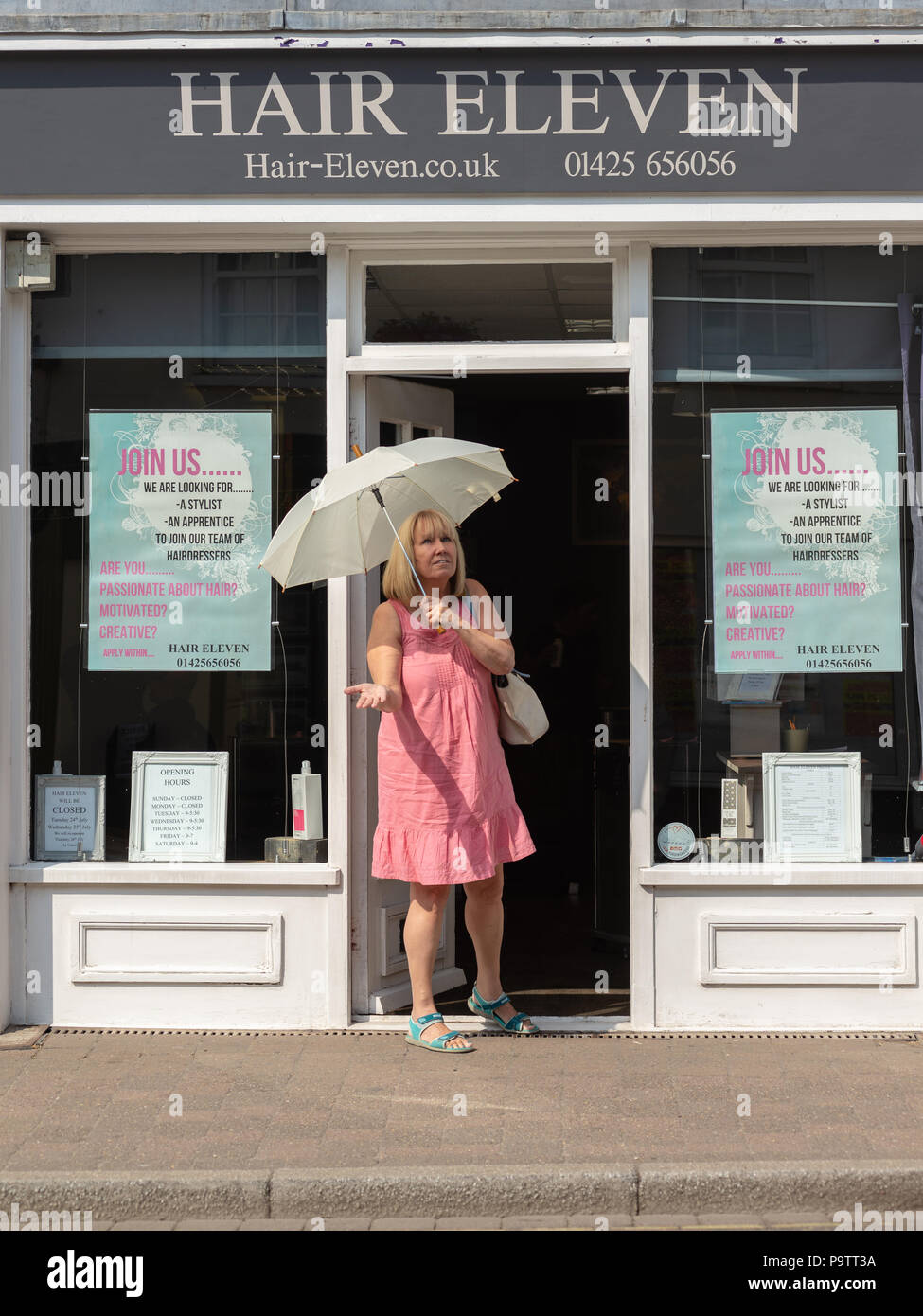 Woman emerging from a hair dressing salon while holding a light umbrella and expecting rain. Stock Photo