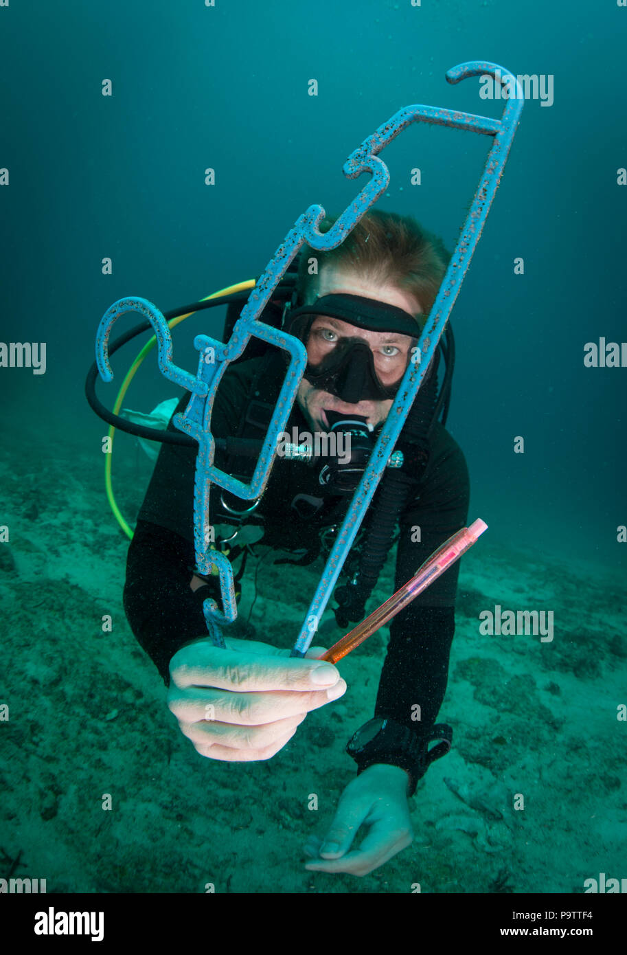 A diver underwater collecting plastic trash on the seabed, holding a discarded coat hanger and a pen, scuba diving at Mabul Island, Sabah, Malaysia. Stock Photo