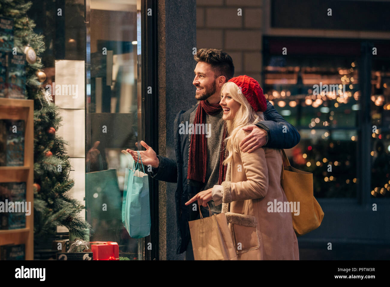 Side view of a couple doing some window shopping at christmas. The mid adult male has his arm around the mid adult female and they are talking about w Stock Photo