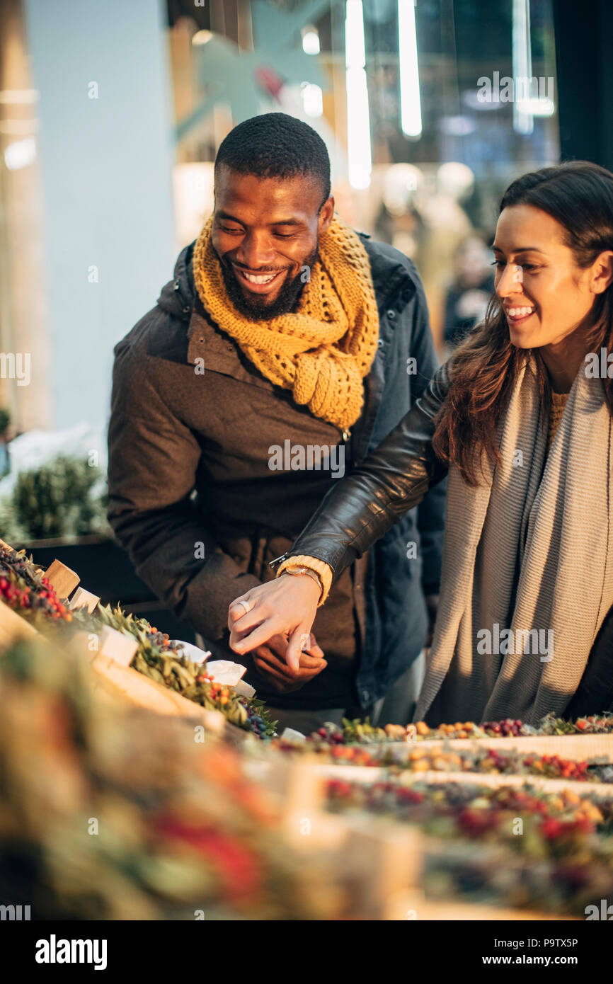 Front view of a couple standing at a christmas market stall deciding on what wreath they should buy. Stock Photo