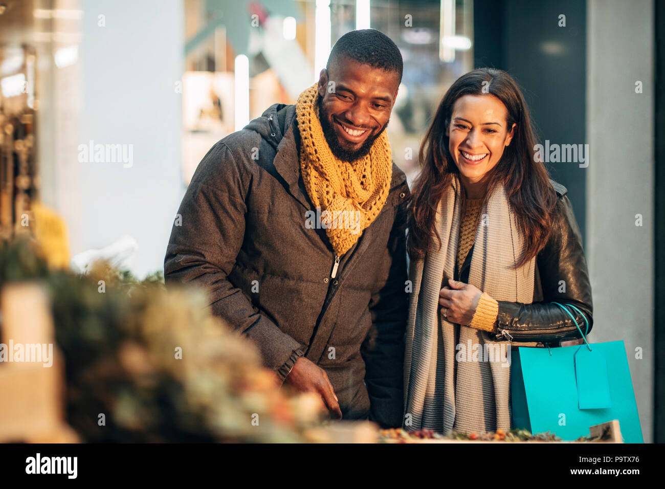 Front view of a couple standing at a christmas market stall deciding on what wreath they should buy. Stock Photo