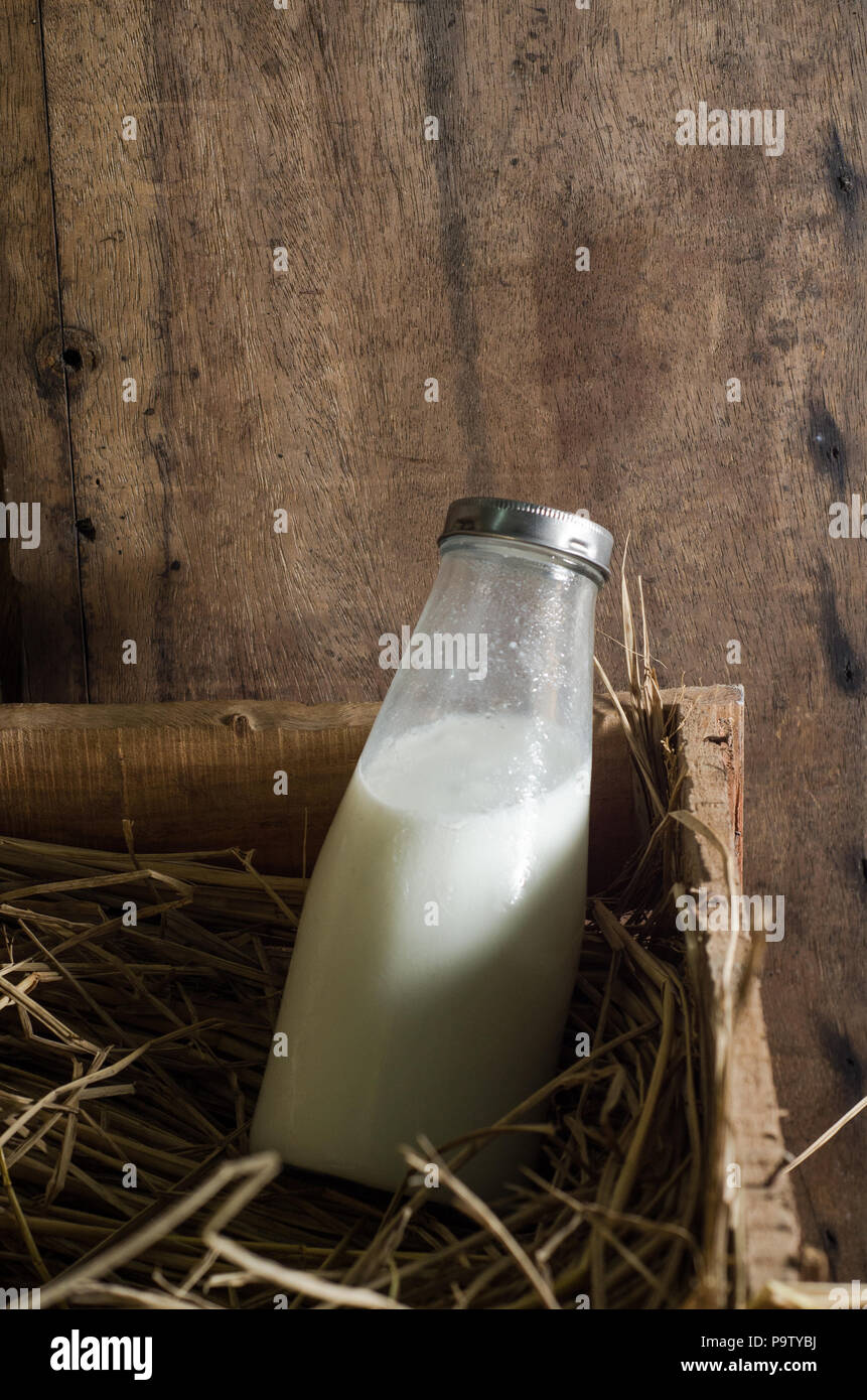 Farm fresh milk in a milk bottle with a wooden background on straw in a wooden chest Stock Photo