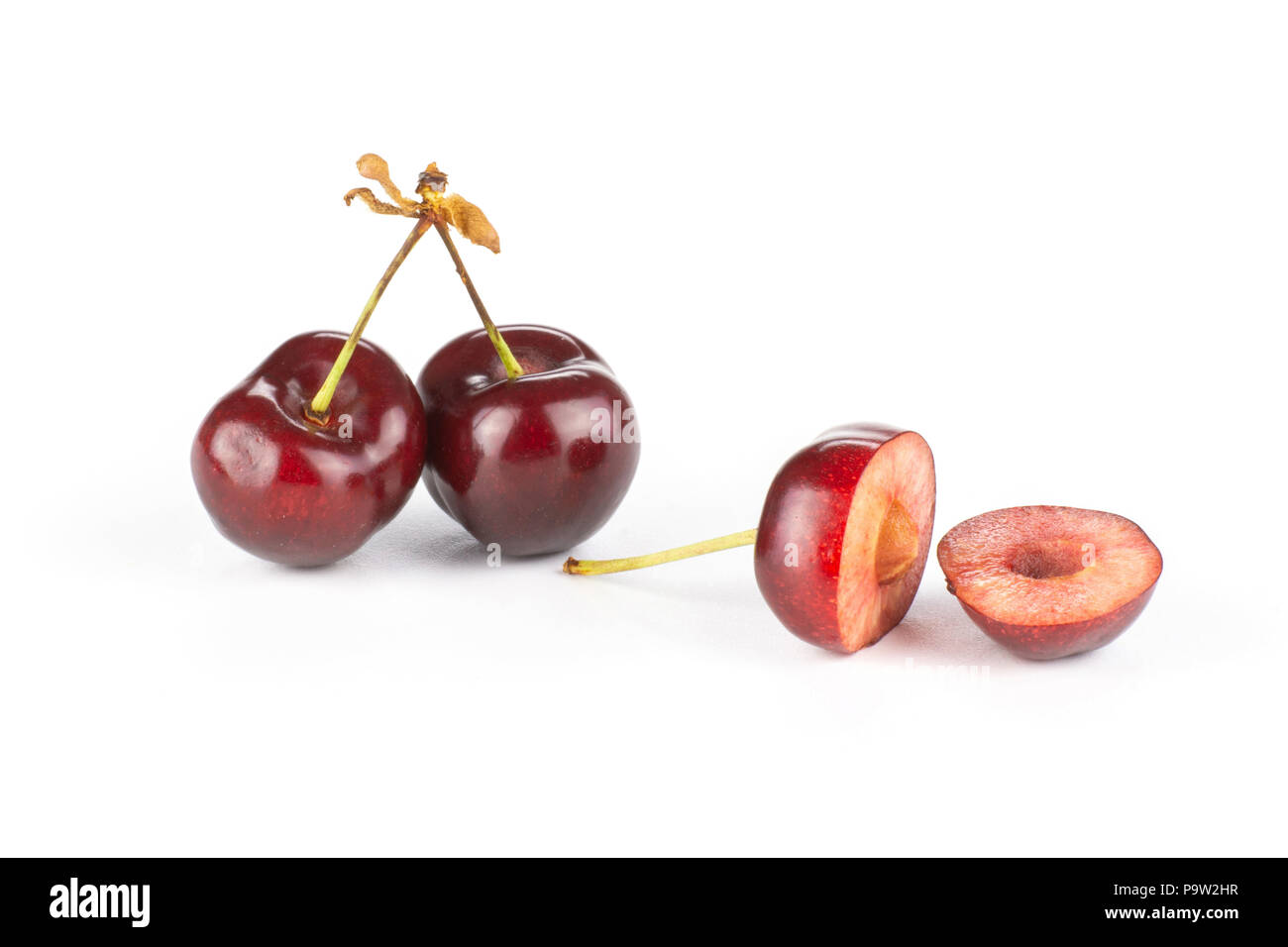 Group of two whole two halves of sweet bright red cherry one cut in halves isolated on white Stock Photo