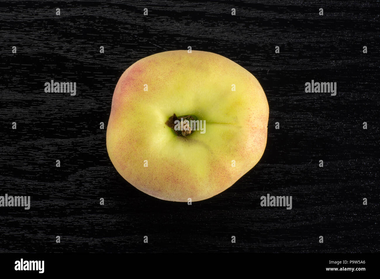 One fresh ripe Saturn peach flatlay on black wood background Stock Photo
