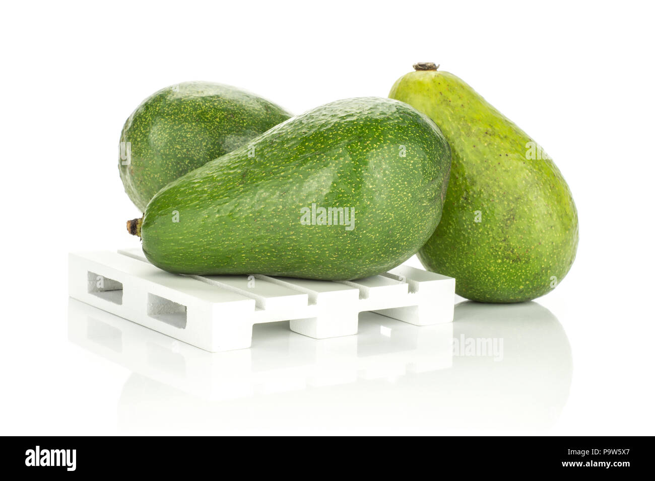 Three green smooth avocado on a wooden pallet isolated on white background ripe shiny bacon variety Stock Photo