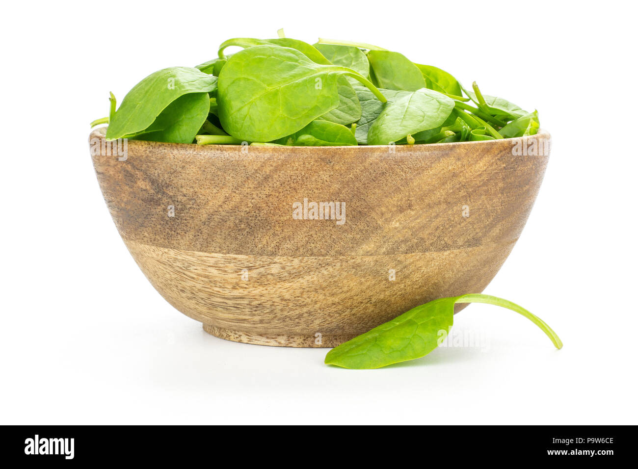 Fresh baby spinach leaves in a wooden bowl and one leaf is near isolated on white background Stock Photo