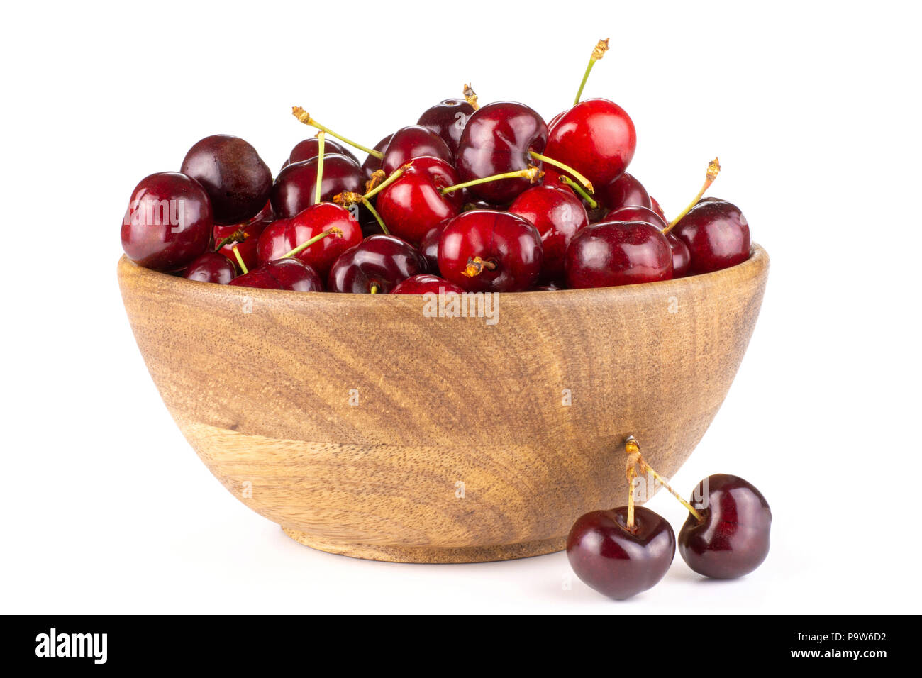 Sweet bright red cherry in a wooden bowl and two is near it isolated on white Stock Photo