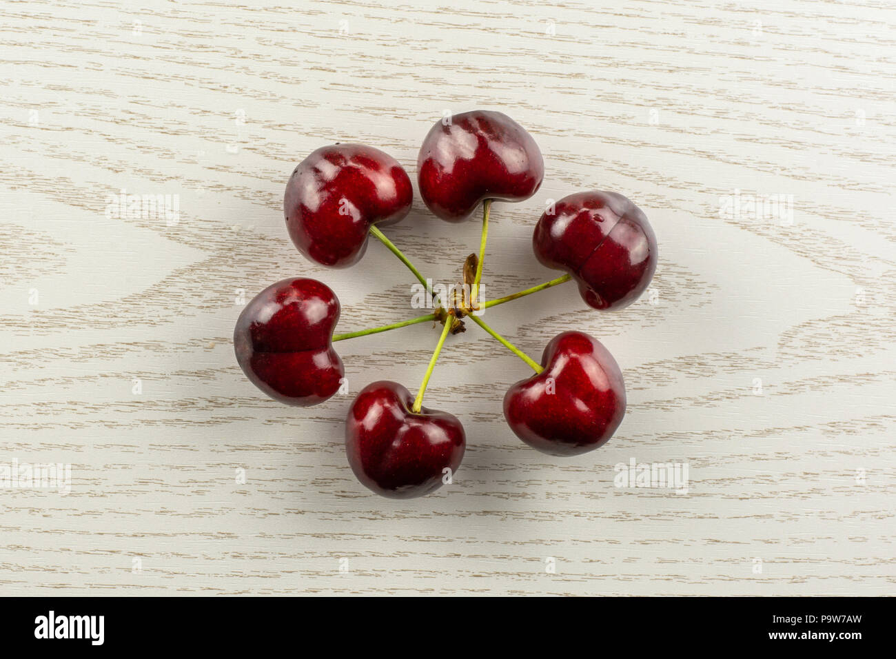 Group of six whole sweet bright red cherry in a circle flatlay on grey wood Stock Photo