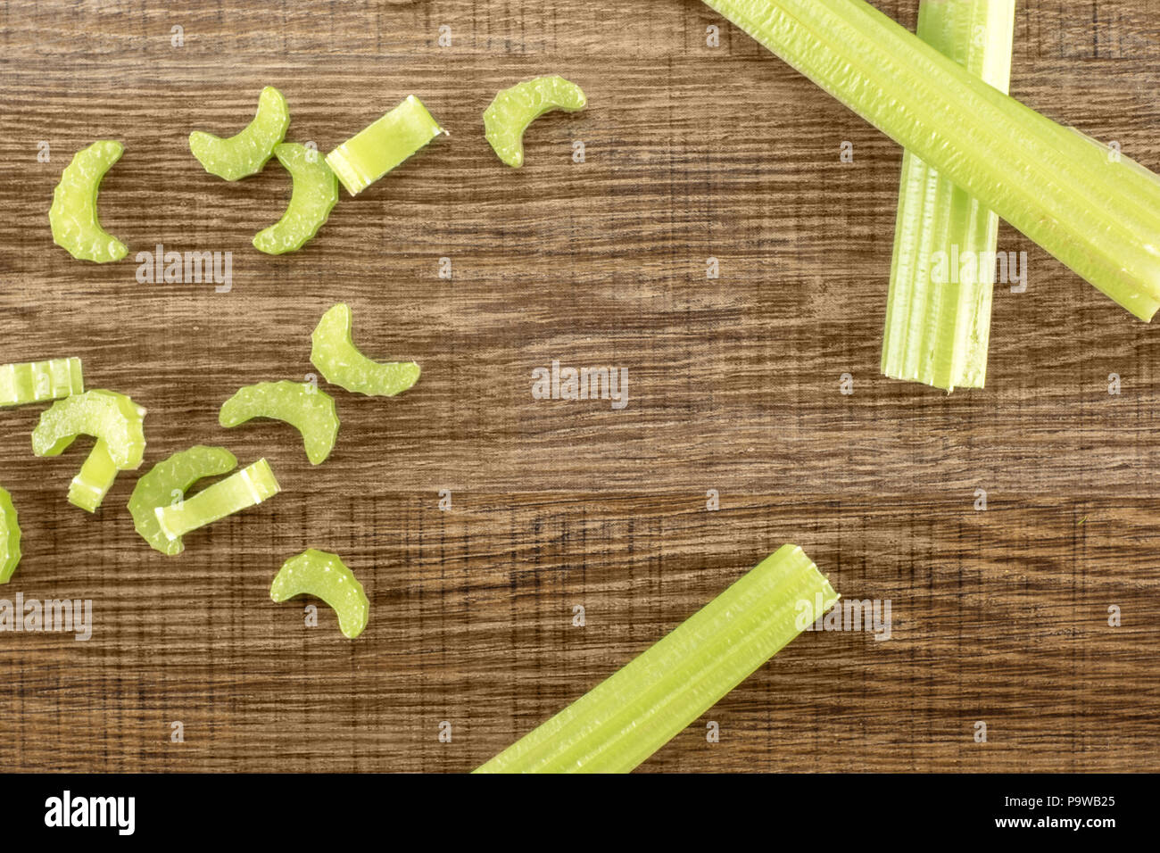 Three green celery sticks with fresh chopped pieces isolated on wooden background Stock Photo