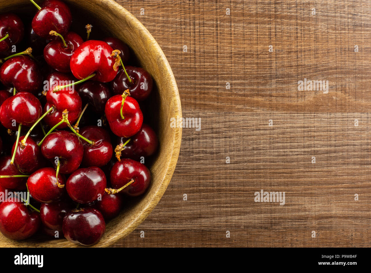 Sweet bright red cherry in a wooden bowl flatlay on brown wood Stock Photo