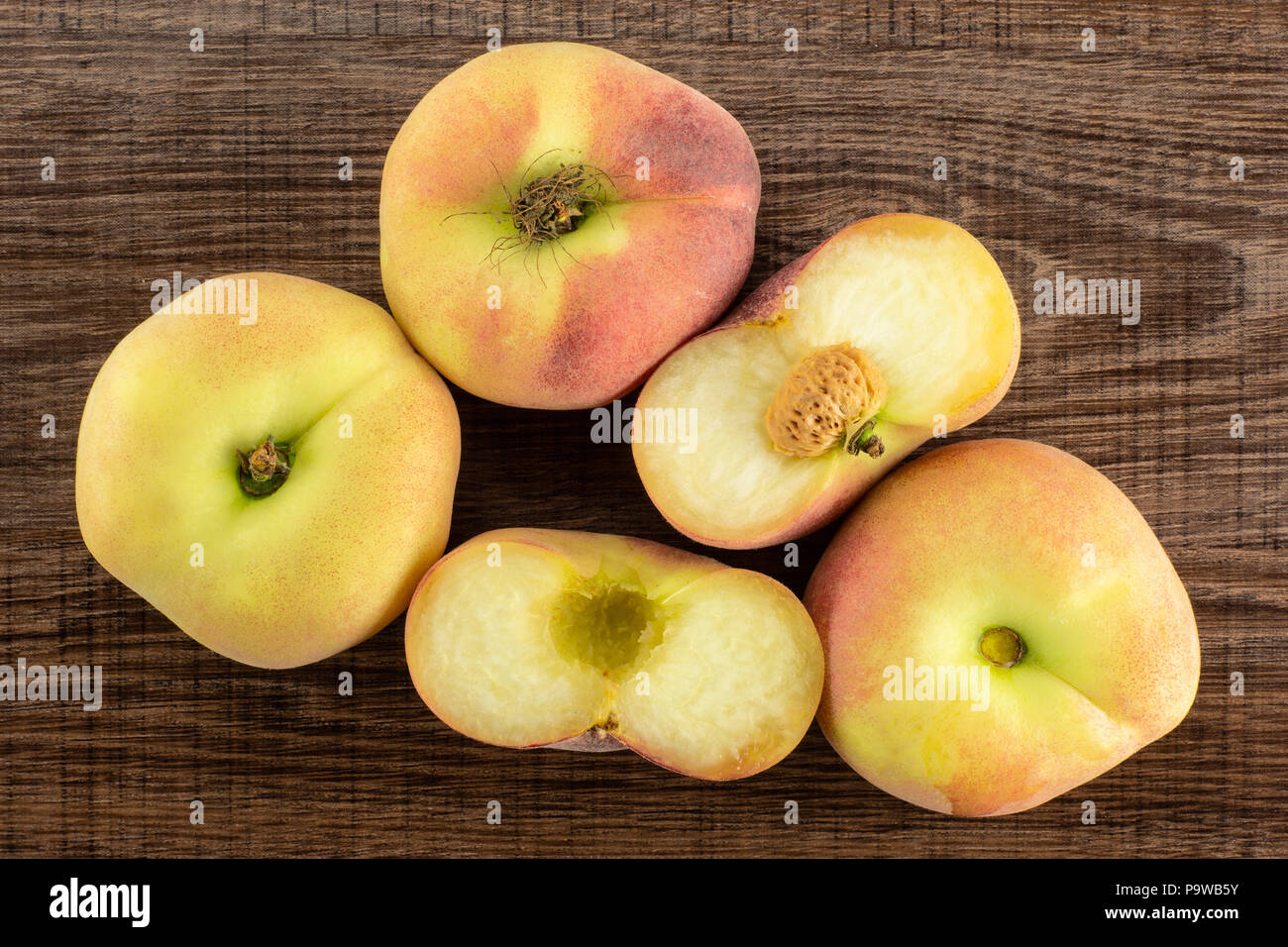 Three fresh ripe Saturn peaches and one cut in two halves top view on