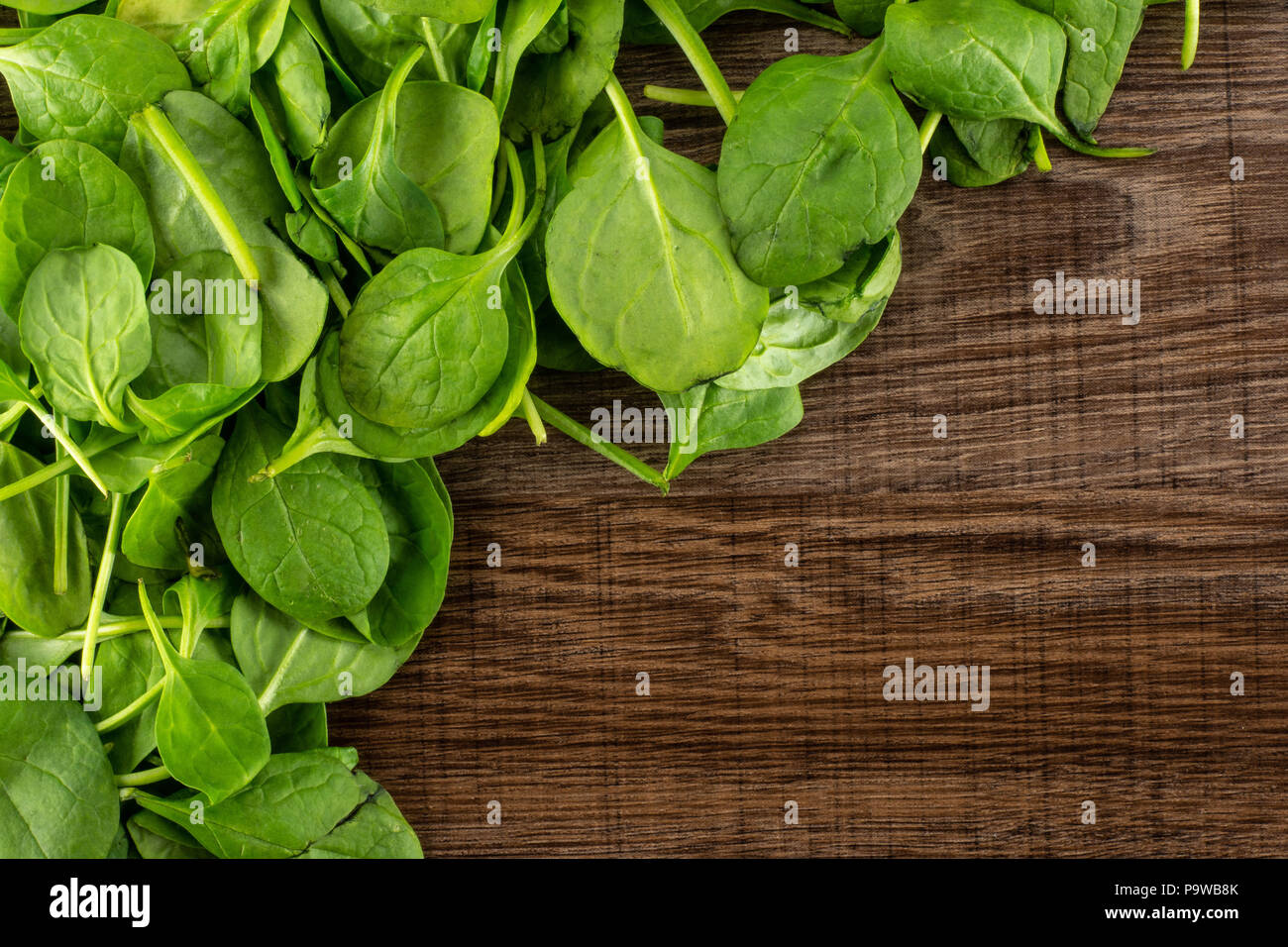 Fresh baby spinach leaves top view on brown wood background left upper corner Stock Photo