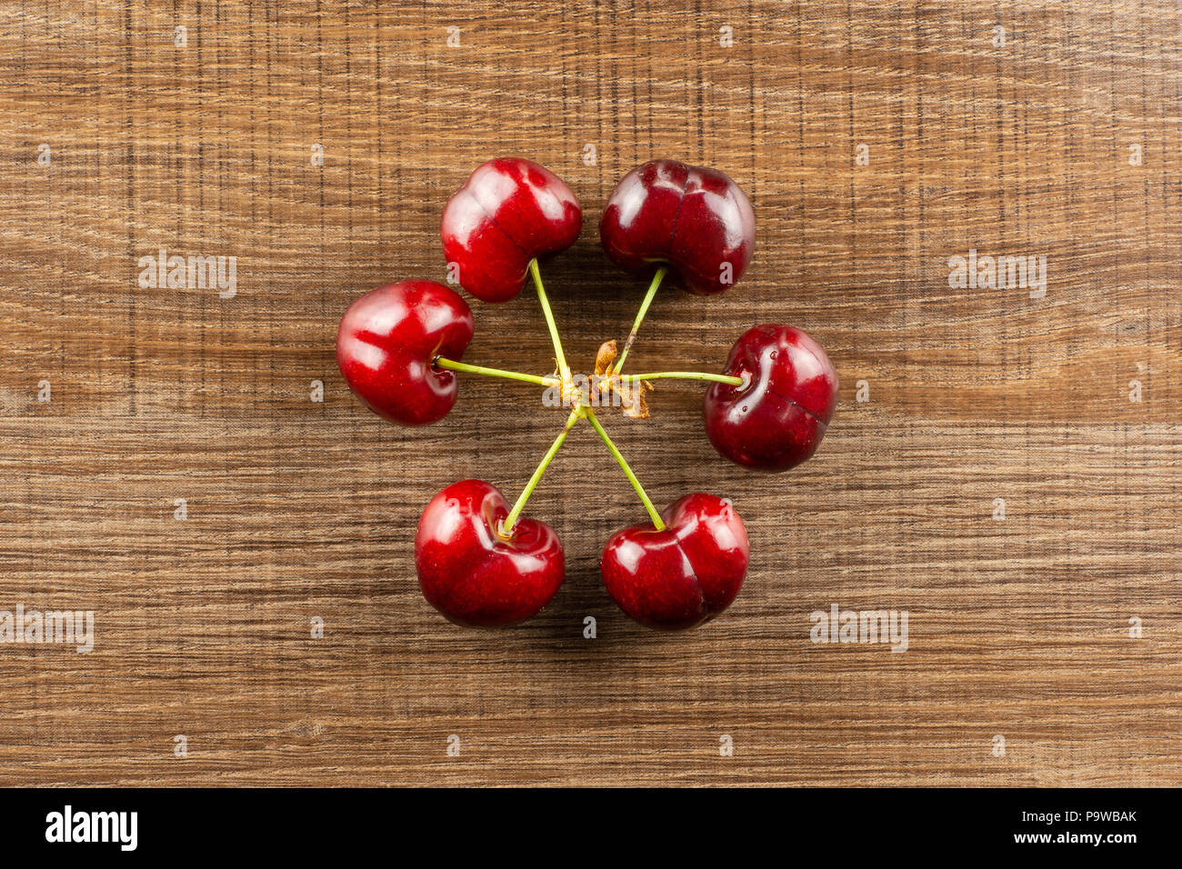 Group of six whole sweet bright red cherry in a circle flatlay on brown wood Stock Photo