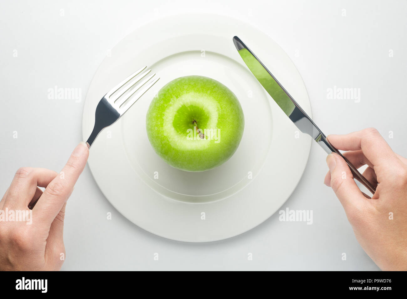 Diet concept, green apple on a white plate, fork, knife, woman c Stock Photo