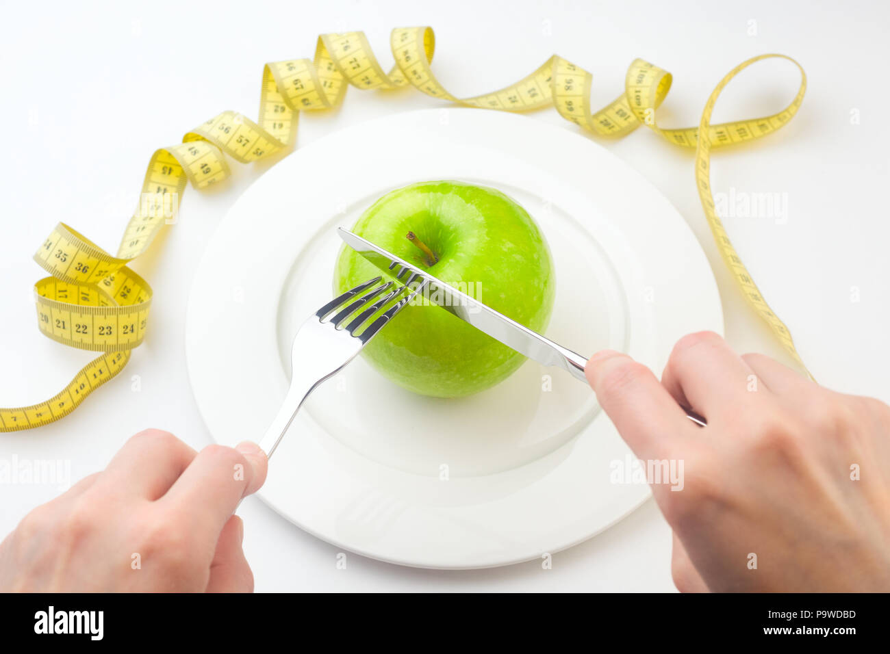 Diet concept, green apple on a white plate, yellow measuring tap Stock Photo
