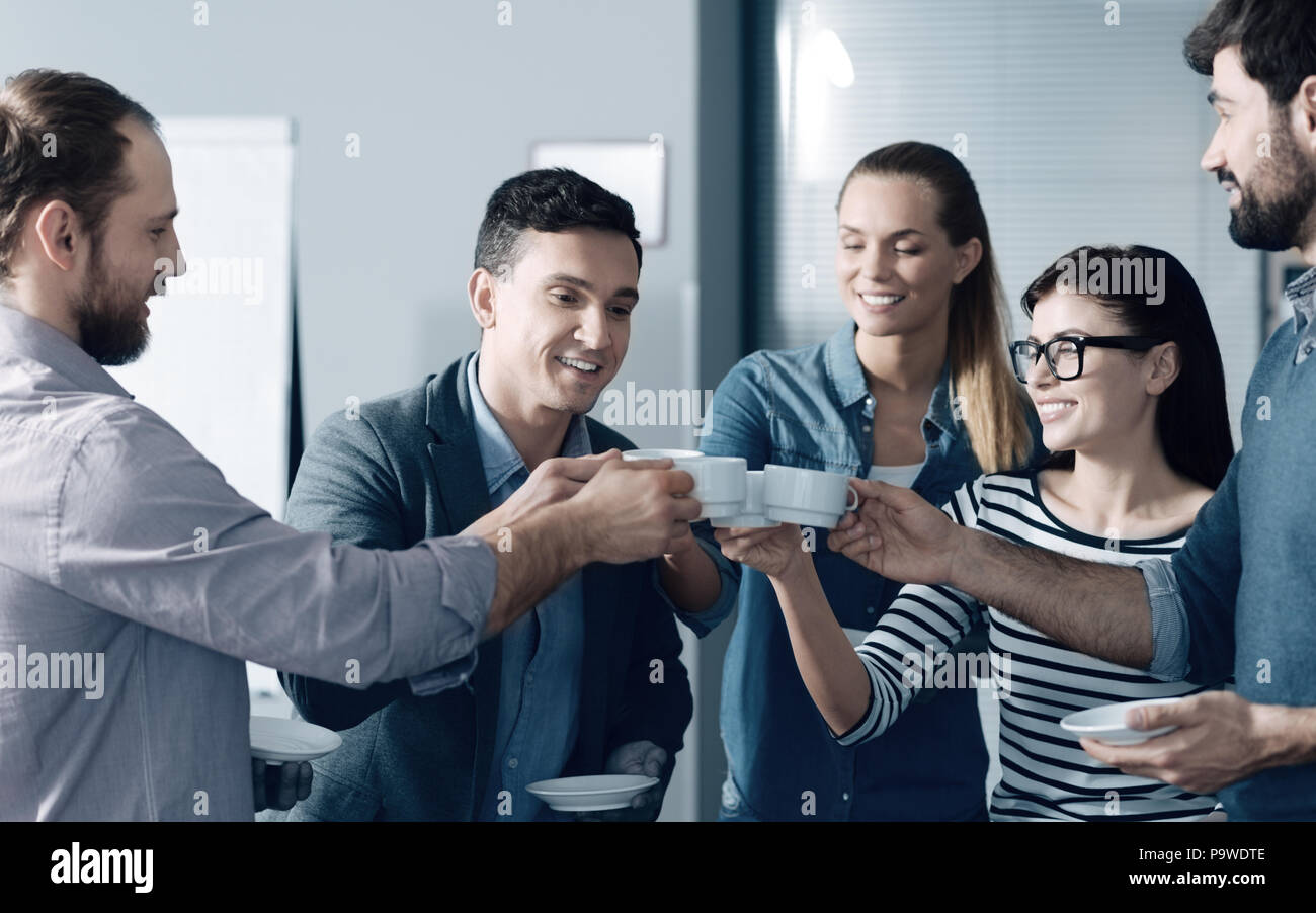 Friendly team. Cheerful smiling young colleagues having a break in the office while drinking coffee and expressing positivity Stock Photo