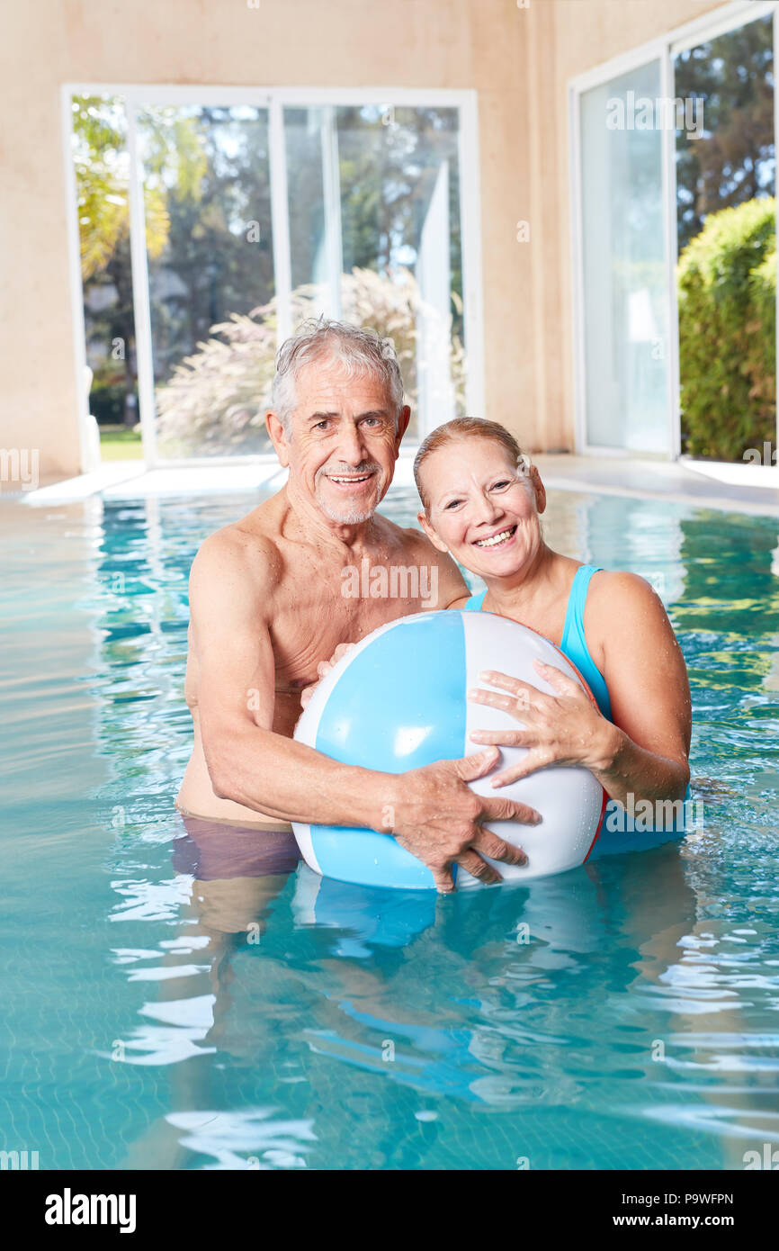 Happy seniors couple with a beach ball in the swimming pool at the spa hotel Stock Photo