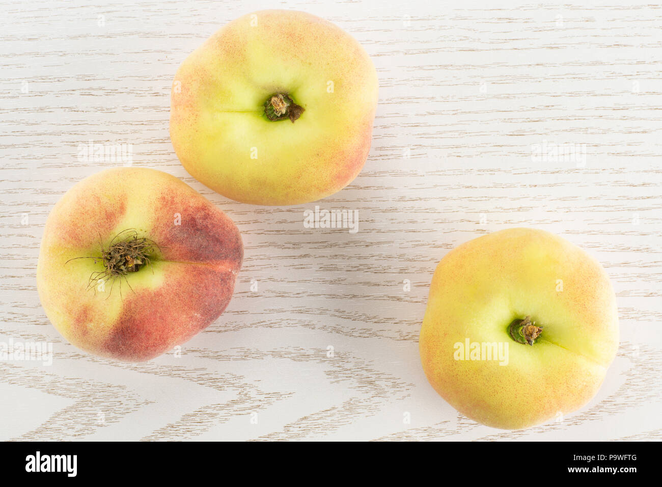Three fresh ripe Saturn peaches top view on grey wood background Stock