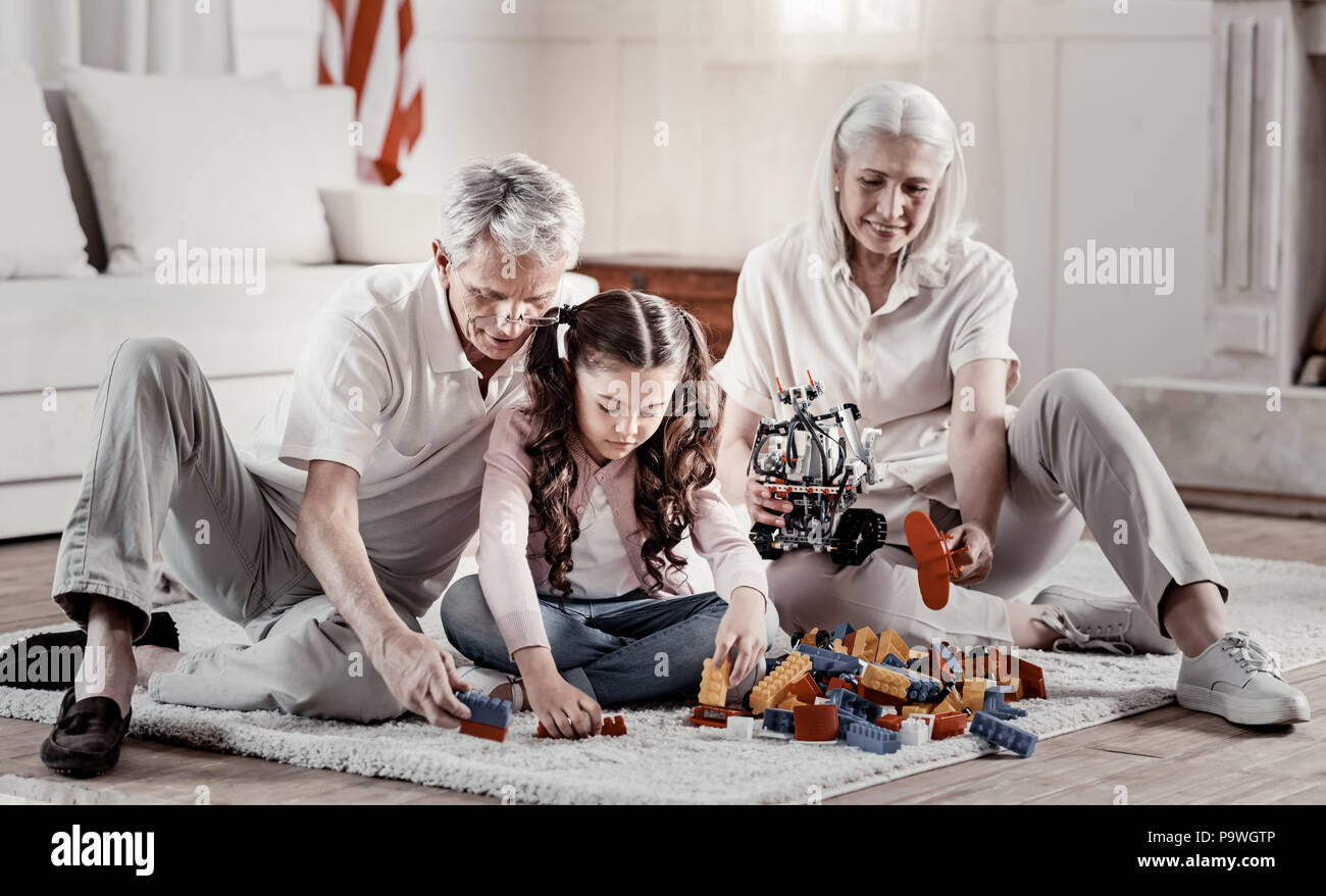 Repeat after me. Warmhearted beaming grandparents sitting on the carpet  playing with lego while concentrated granny carrying robot Stock Photo -  Alamy