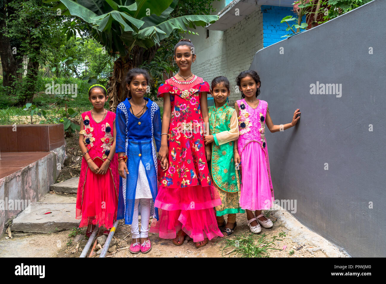 A group of little girls in traditional Indian costumes stands against a background of trees and a gray wall. Indie June 2018 Stock Photo