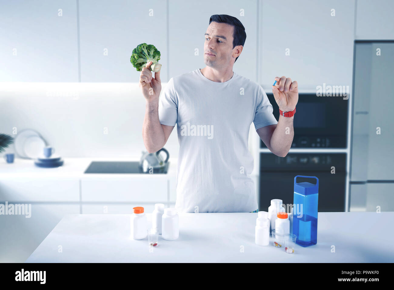 Progressive man having a lot of medicaments and looking at the broccoli Stock Photo
