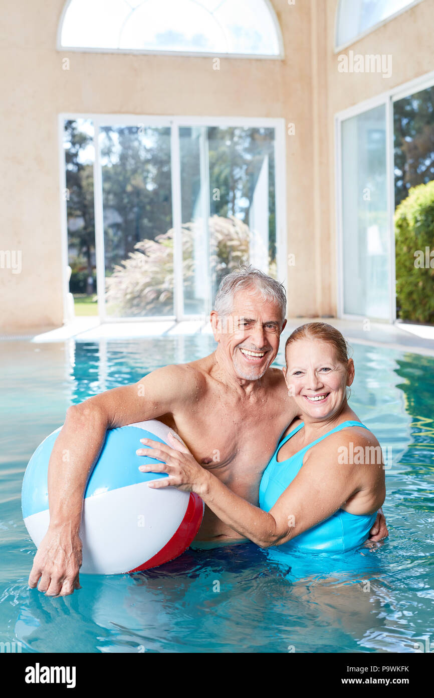 Happy seniors couple in pool of spa wellness hotel with beach ball Stock Photo