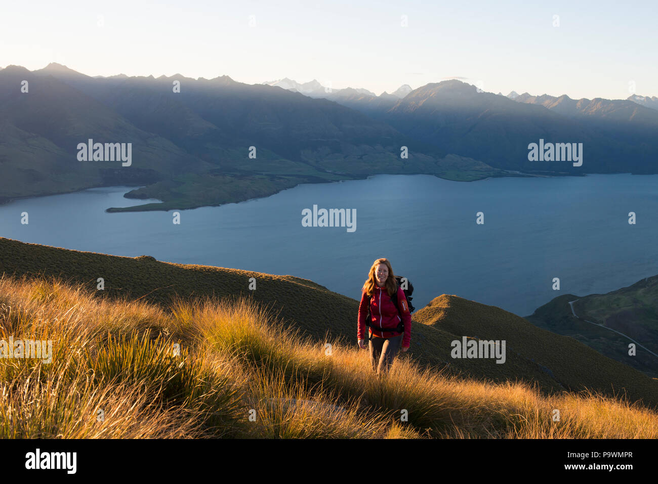 Female hiker at Isthmus Peak, Lake Wanaka and mountain panorama at atmospheric evening light, Otago, South Island, New Zealand Stock Photo