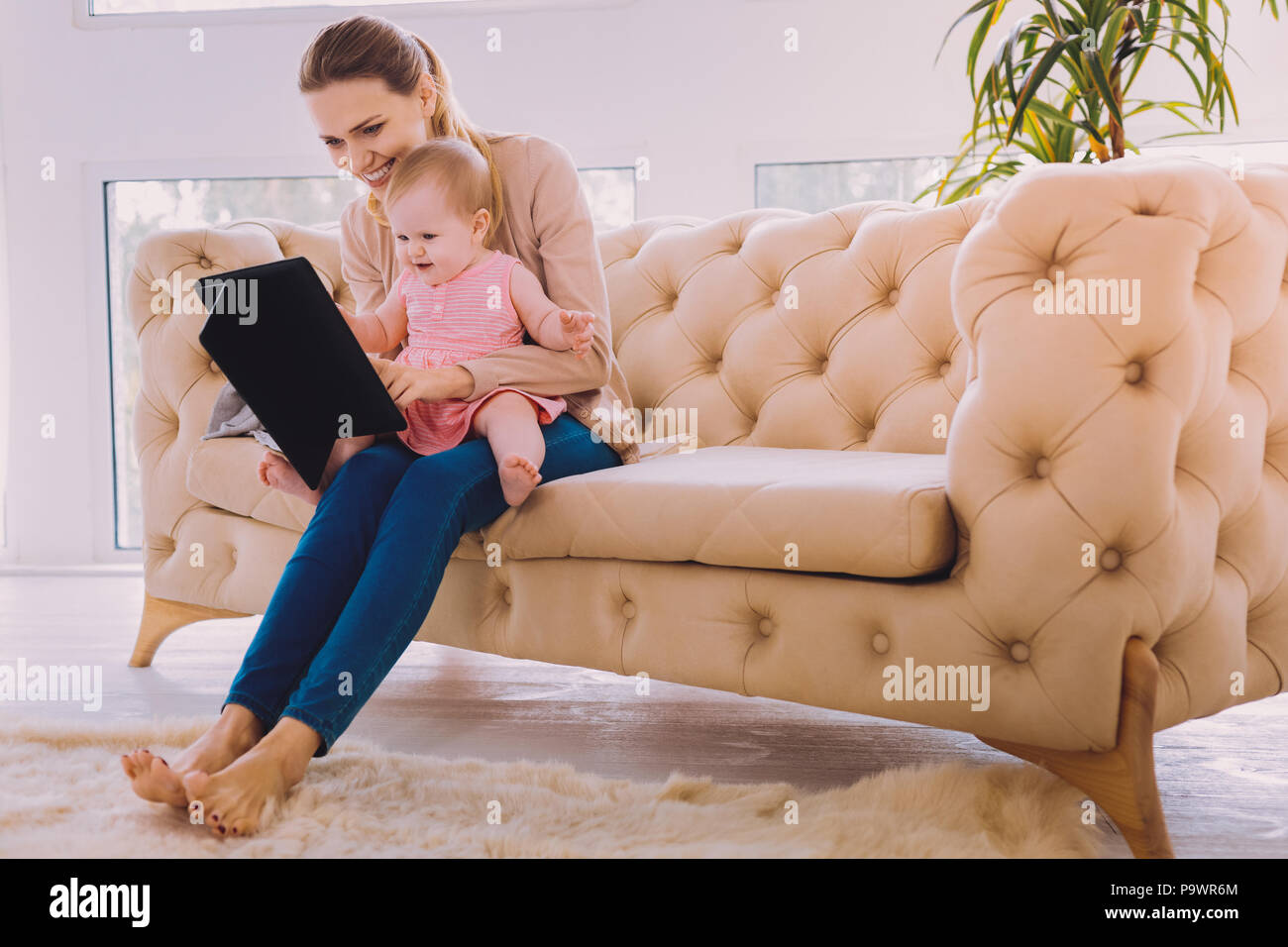 Watching cartoons. Cheerful kind young mother holding a modern tablet while showing funny cartons to her little child Stock Photo