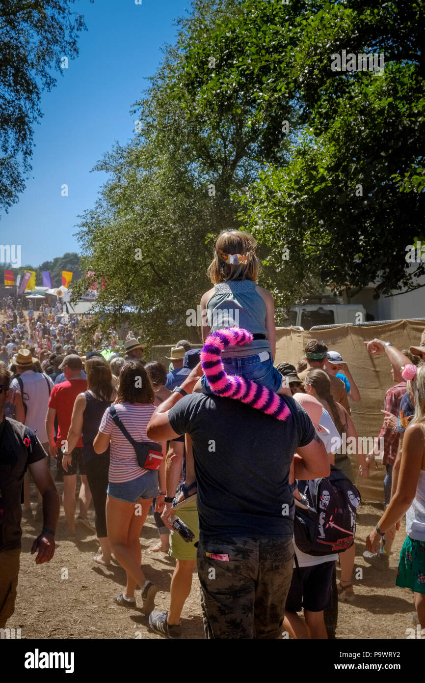 Child with pink and purple striped tiger tail sits on a man's shoulders as they walk in the crowd from the Sunrise Bridge up towards the main festival Stock Photo