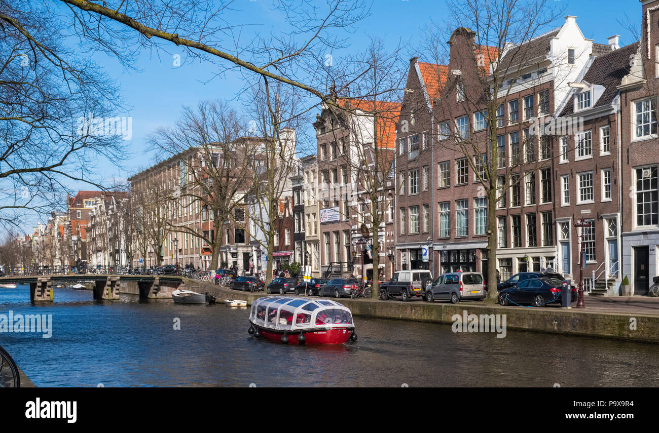 Amsterdam tall narrow canal houses and a sightseeing tourist cruise boat on a canal, The Netherlands, Europe Stock Photo