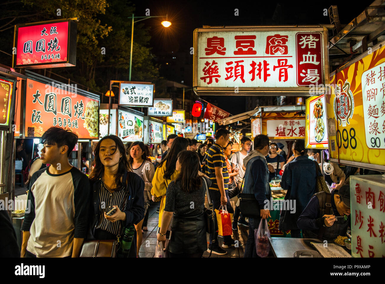 A bustling night food market in Taipei city, Taiwan, with many Mandarin signs and people walking past. Stock Photo
