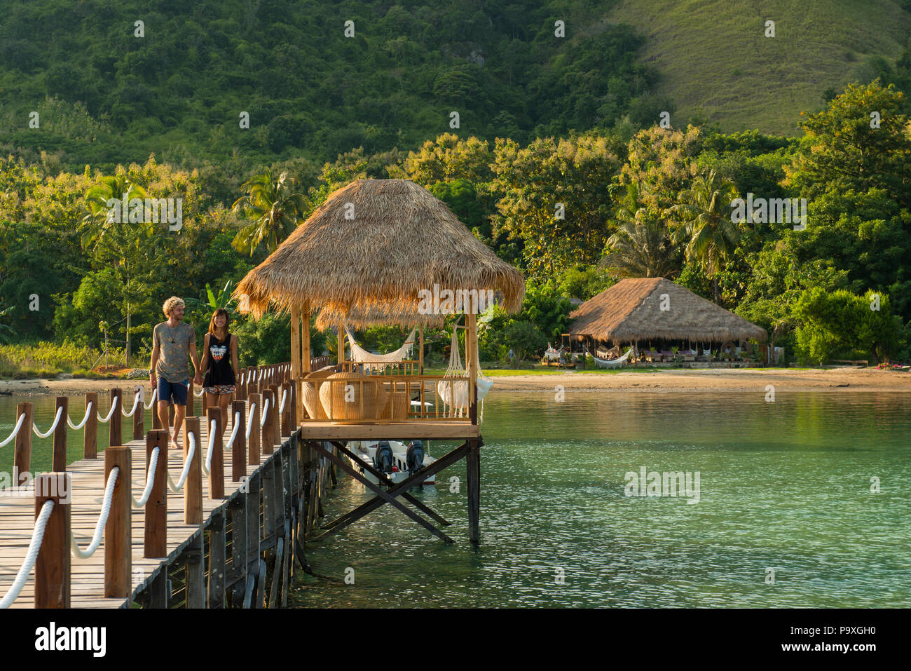 A young tourist couple walking along the jetty of a dive resort in early morning sunlight - Scuba Junkie Komodo Beach Resort, Flores, Indonesia. Stock Photo