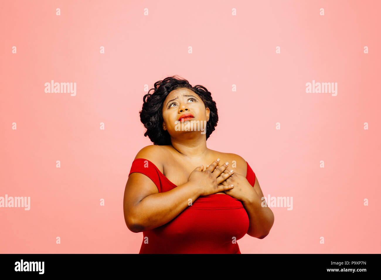 Woman holding her chest and looking up full of emotion, isolated on pink background Stock Photo
