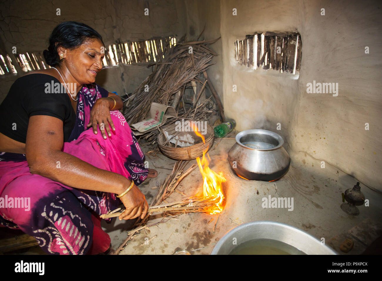 A villager woman in a remote subsistence farming village on an island in the Sundarbans, the Ganges Delta in eastern India that is very vulnerable to sea level rise. She is cooking on a traditional clay oven, fueled by biofuel (rice stalks), low carbon cooking. Stock Photo