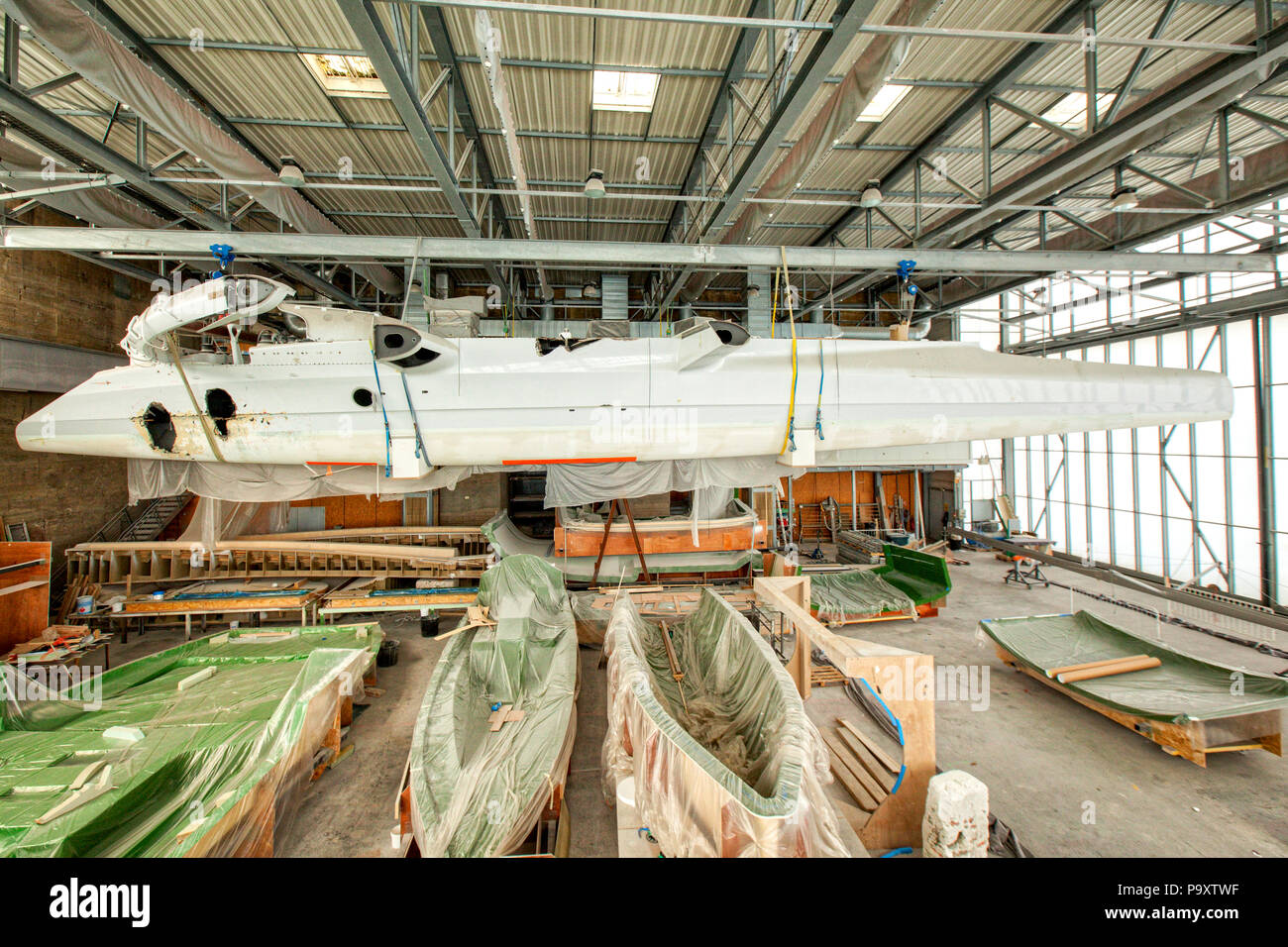 Trimaran racing yacht suspended from roof of a boat shed, Keroman, Submarine Base, Lorient, Morbihan, Brittany, France. Stock Photo
