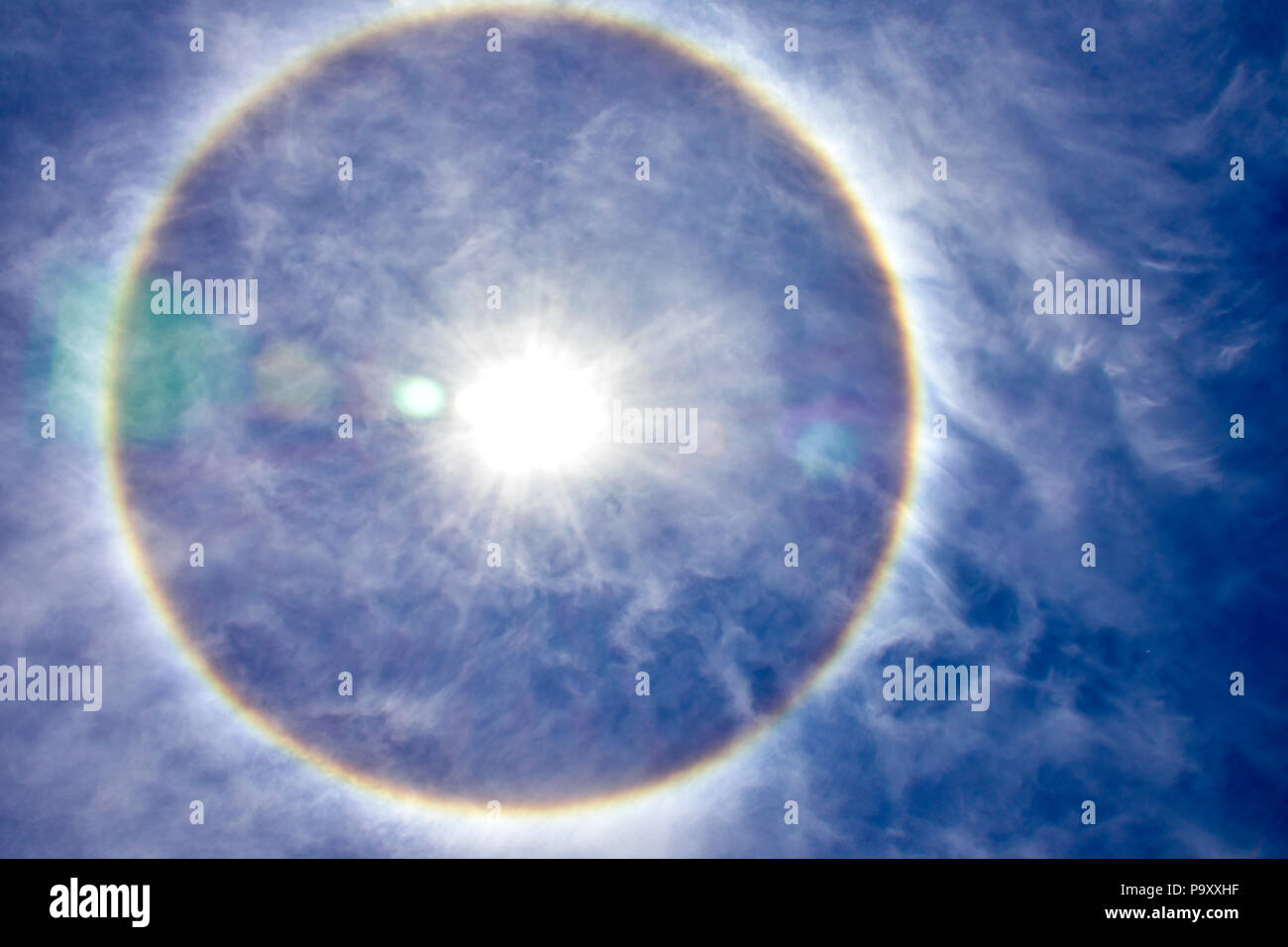 Solar halo in a sunny summer midday. Blue sky with white clouds and an halo with the rainbow colors around the sun. Stock Photo
