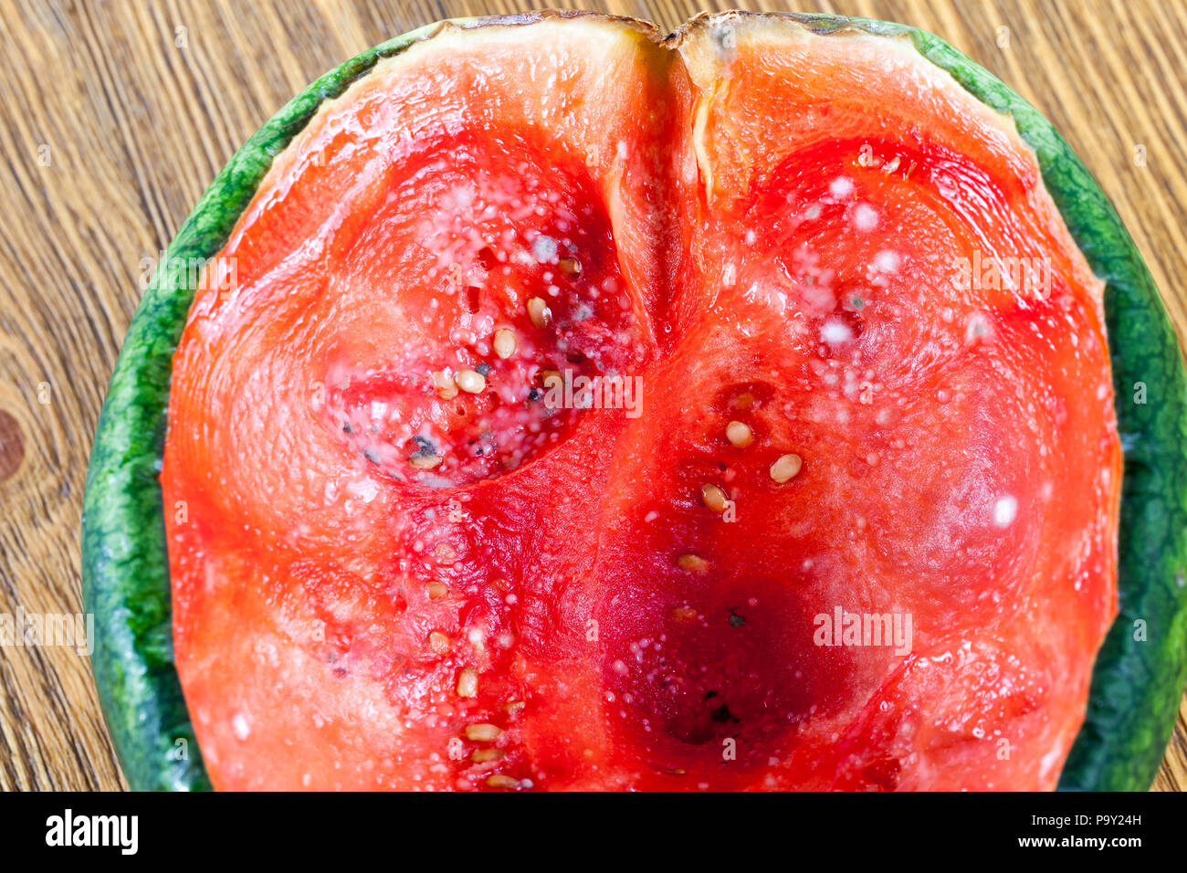 red juicy pulp of ripe watermelon of small size, covered with mold, dangerous food closeup Stock Photo