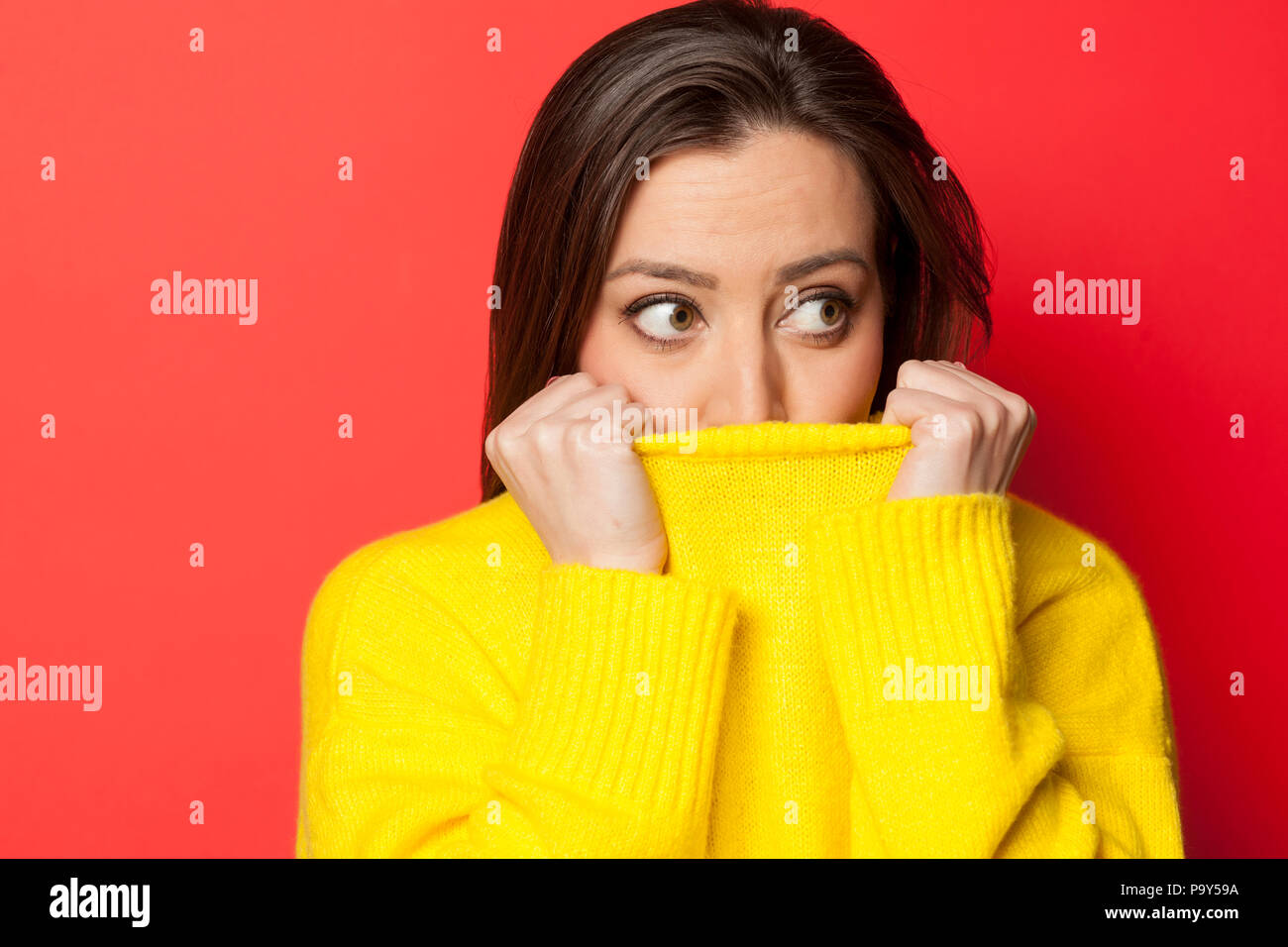 beautiful affraid woman in a yellow sweater on a red background Stock Photo