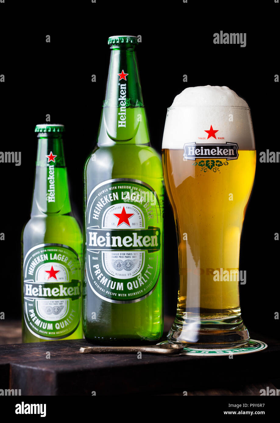 LONDON, UK - APRIL 27, 2018: Bottles and original glass of Heineken Lager Beer on dark wooden background. Heineken is the flagship product of Heineken Stock Photo